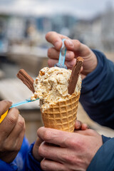 A close up of hands holding an ice cream cone and scooping the ice cream with spoons