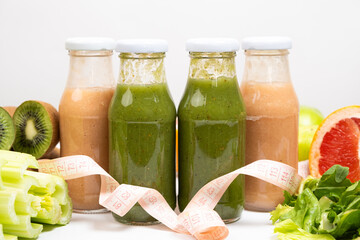 Healthy bottled smoothies among vegetables and fruits and measuring tape.