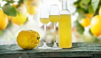 Bottle limoncello and two glasses standing on weathered wooden table. Atmospheric background still...