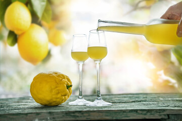 Limoncello poured into glasses standing on weathered wooden table. Atmospheric background still...