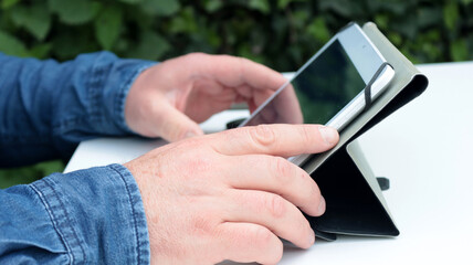 close-up of a man's hands holding his tablet in the garden