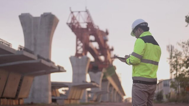 A man in a yellow jacket is writing on a clipboard while standing in front of a bridge. Concept of work and productivity