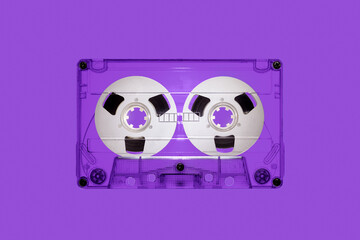 Clear plastic retro audio cassette with spools, isolated on violet background in close up. The picture is intended for design work on the theme of music - obrazy, fototapety, plakaty