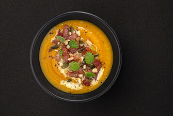Pumpkin cream soup with pumpkin seeds and crispy bacon on black background with copy space, top view