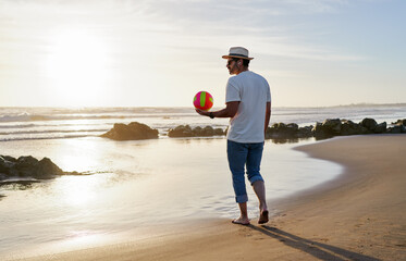 rear view fit mature man walking on the beach holding a beach volleyball ball
