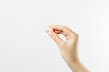 hand holding a round pink pill on a white background. health care concept