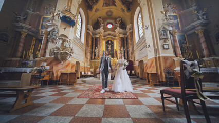 The bride and groom walk through a Catholic church.
