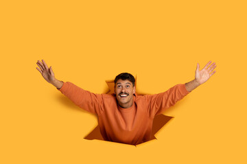Joyful Man Emerging Through Yellow Paper Background With Arms Outstretched
