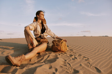 Woman Sitting on Sand in Desert with Hand on Shoulder and Bag, Peaceful Moment in Arid Landscape...