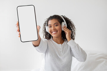Smiling Young Woman Displaying Smartphone Screen While Wearing Headphones