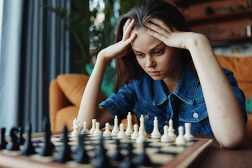 Woman contemplating her next move in intense chess game at table, head in hands, deep in thought