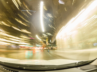 Long exposure of fast car at night traffic lights in the rainy evening. Fog diffusion. City life downtown, urban lights trails on highway, road transport. Travel on high way during night and rain.