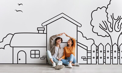 Cheerful asian couple sitting on floor with hand-drawn house