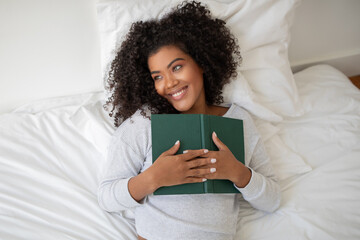 Woman Laying in Bed Holding a Book, Looking Away
