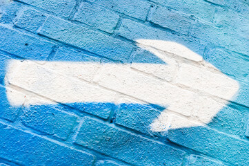 White arrow graffiti sprayed on blue brick wall