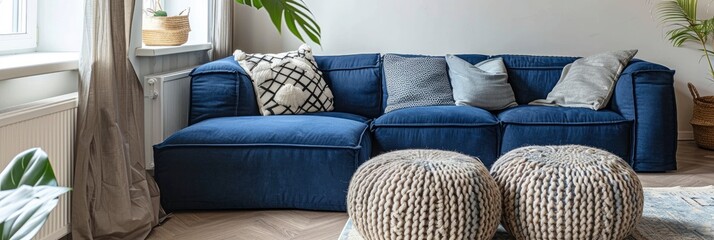 A navy blue corner sofa with grey cushions and two knitted beige footstools for a modern living room - obrazy, fototapety, plakaty