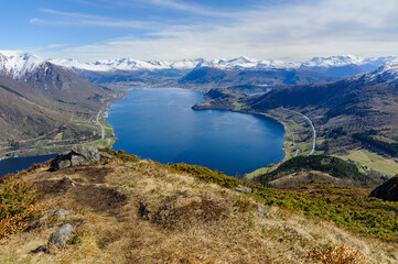 Overlooking a tranquil fjord, mountains rise in the distance beneath a bright, expansive sky.