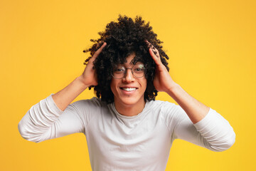 Surprised young curly-haired black guy clutching his head,
