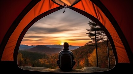 A man enjoys the view of the autumn mountains while sitting in a tent. Hiking and digital detox concept. Contemplation of nature alone with your thoughts. Peace and slow life. Alone with yourself