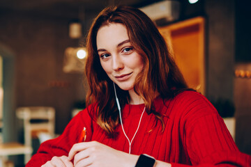 Portrait of teen hipster girl doing homework listening music from smartphone playlist in cafe,...