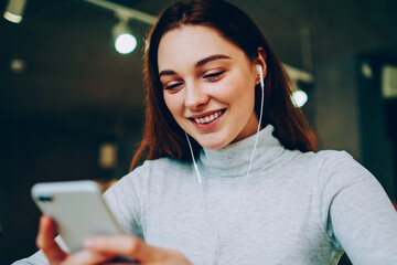 Cheerful teen girl watching favorite serial on smartphone via good wifi connection in cafe, smiling...