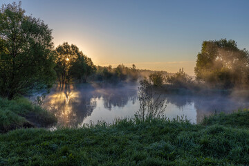 Blue fog over the river, the rising sun reflected in the water, foggy morning in the countryside.