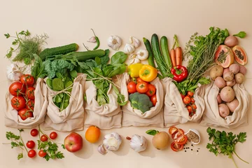 Fotobehang A variety of fresh organic fruits and vegetables, along with vegan meal ingredients, neatly packed in reusable eco cotton bags on a beige background. This setup exemplifies zero waste shopping  © Aleksandra