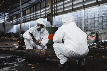 Workers in protective suits inspect chemicals in an old factory, safeguarding against hazards and...