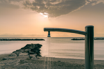 The outdoor beach shower is set against the beautiful backdrop of the sea sunrise, embodying...