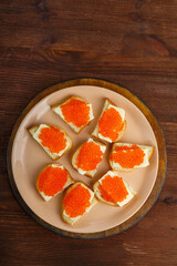 Canapes with red caviar on a plate on a wooden table. copy space