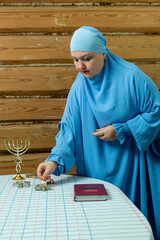 A Jewish woman in a blue veil lights candles in Magen David candlesticks in honor of Shabbat