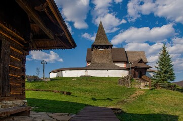 Fototapeta na wymiar Old wooden historic fortified church, sunny day during early spring, blue sky with clouds. The village of Cerin near Banska Bystrica, Slovakia
