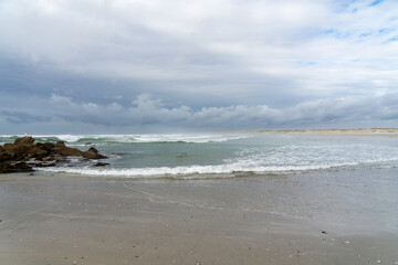 Sable mouillé, rochers, mer agitée sous un ciel couvert à la plage de la Torche en Bretagne, un tableau saisissant de la nature sauvage de la région.