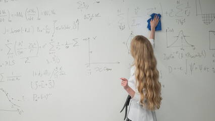 Caucasian woman erasing formulas from white board. 