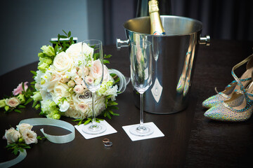 Champagne, wine glasses, wedding shoes and a bouquet on the table