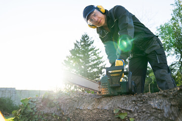 A man in uniform cuts an old tree in the yard with an electric saw.