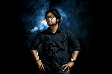 concept portrait photo of a man with a serious expression and hands on his waist on a black background and using smoke, with low lighting techniques