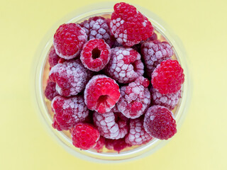 raspberries frozen in a glass dish top view, yellow background
