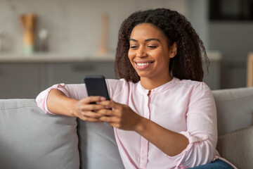 Happy young black woman using smartphone at home