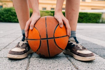 A teenage boy holds a ball with his feet after playing basketball.