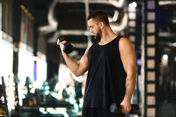 Muscular Man Performing Dumbbell Curls at Modern Gym