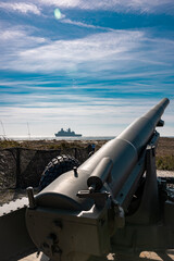 cannon on the beach With a large military ship in the background 