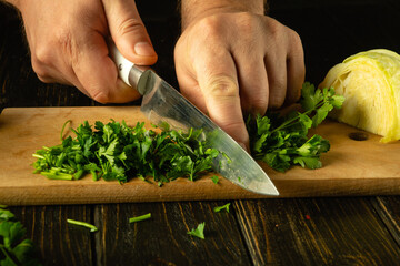 Close-up of a chef hands cutting green parsley with a knife on a cutting board for preparing a...