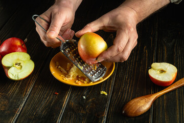 Preparing apple tart on the kitchen table. The chef hands grate an apple for a vegetarian dish.