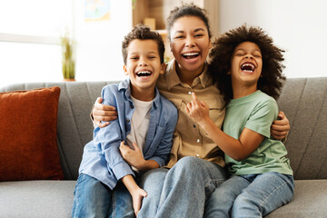 Happy mother and two kids sitting on the sofa in room at home, embracing, looking at camera