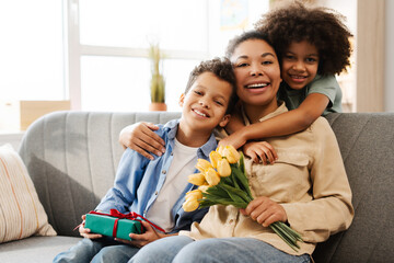 Happy African American family hugging, mother with bunch of flowers and gift box at home