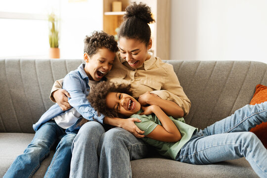 Happy two kids and their mother having fun while fooling around together, sitting on sofa at home
