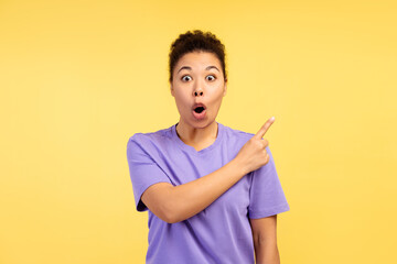 Portrait of surprised young woman, model, looking at camera, pointing finger at copy space