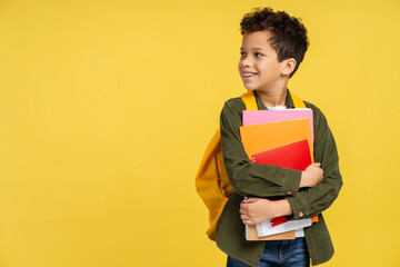 African American pupil with backpack, holding books, looking to side, isolated on yellow background