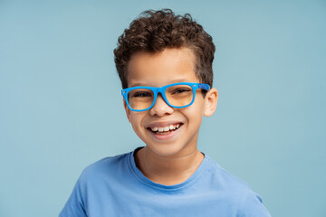 Little boy wearing stylish eyeglasses looking at camera, isolated on blue background
